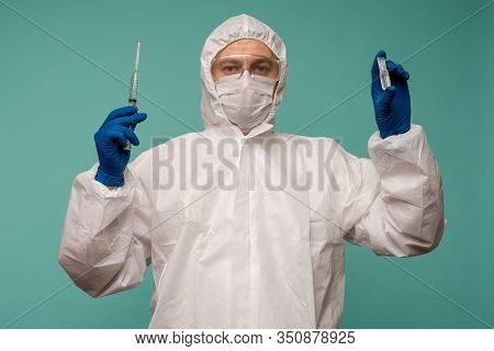 A Male Doctor In Protective Overalls And A Mask Holds An Ampoule With A Vaccine And Syringe In His H
