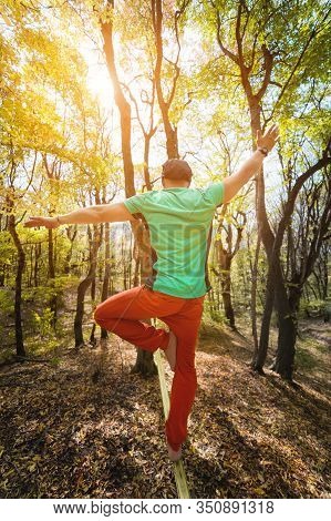 Wide Angle Male Tightrope Yogi Balances On One Leg In Heron Pose Barefoot On Slackline In Autumn For