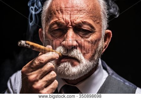 Portrait Of Serious Senior Man Who Is Smoling Cigar.