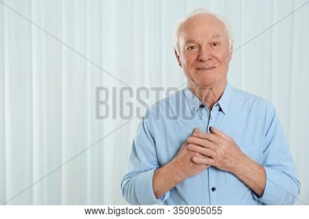 Grateful Senior Man With Hands On Chest Against Light Background. Space For Text
