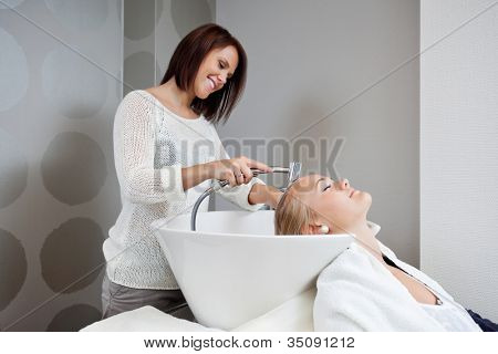 Kosmetička s úsměvem při mytí vlasů žen zákazníka v beauty salonu