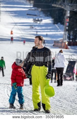 Father And Son Walking On Snow In Ski Resort On Sunny Day