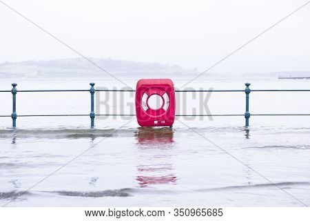 Sea Flood Onto Street With Red Life Safety Ring During Bead Extreme Rain And Weather Storm In Uk