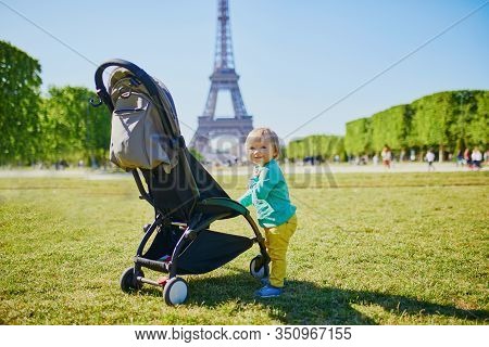 Adorable Happy Baby Girl Standing Next To Her Pushchair In Paris Near The Eiffel Tower. Smiling Todd