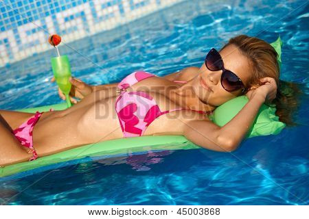 Ragazza sexy in bikini rilassante sull'acqua in estate, posa sul materassino in piscina.