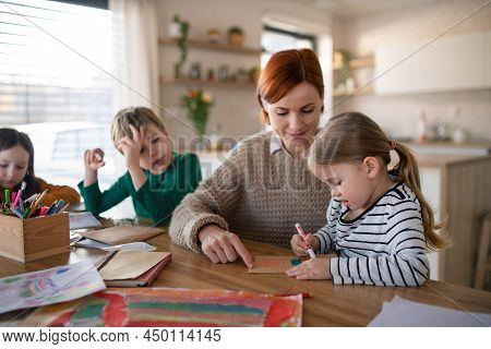 Mother Of Three Little Children Supervising Them When Diong Homework At Home.