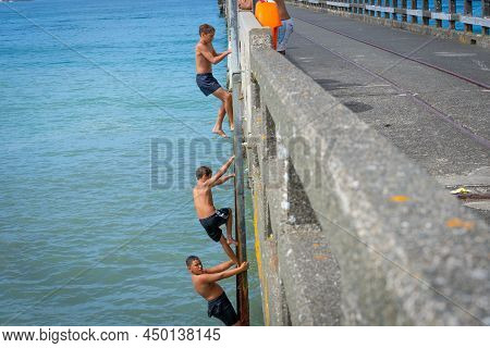 Tolaga Bay New Zealand - February 5 2022; Three Local Boys Climbing Up Ladder And Jumping Of Tolaga 