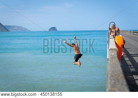 Tolaga Bay New Zealand - February 5 2022; Local Boys Jumping Of Tolaga Bay Wharf Under Encouragement