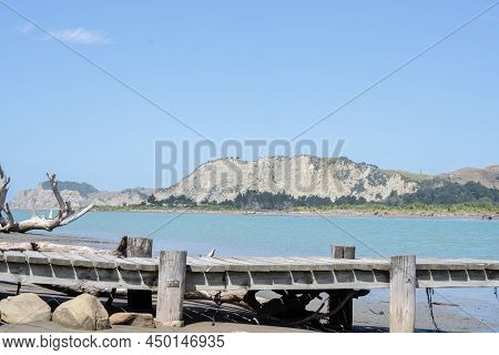 Driftwood Log And Jetty  On Muddy Edge Of Uawa River Running Through Township Of Tolaga Bay.