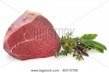 Filete de carne de vaca con ramitas de hierbas frescas sobre fondo blanco.