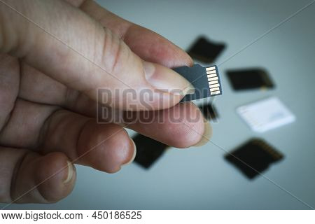Microsd Memory Card In Hand Against A Blurred Background Of Other Sd Memory Cards.