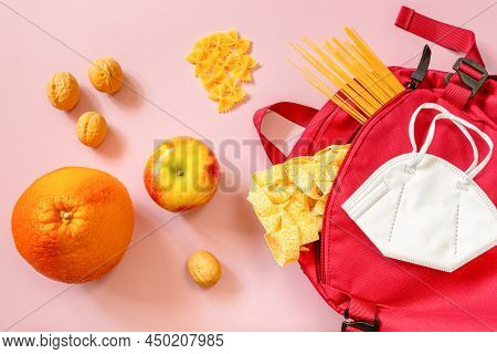 A Red Backpack With Various Pasta, Fruits And Nuts And Protective Mask On A Pink Background. Food De