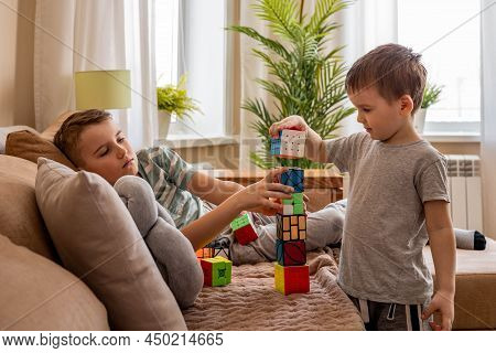 Funny Male Kids Building Tower From Different Rubiks Cubes Playing Together On Couch At Home