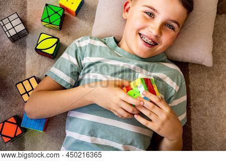 Cheerful Male Adolescent Resting On Comfortable Pillow Floor Assembling Multicolored Rubiks Cube