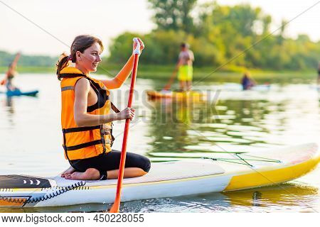 Woman In Life Jacket Sit At Sub Board At River Ar Evening , Forest Trees Background