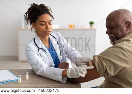 Black Mature Man Getting Vaccinated, Doctor Applying Adhesive Bandage