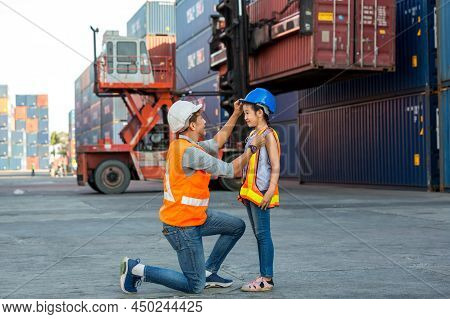 Father Puts A Safety Helmet On Little Daughter At Container Cargo Site. Business Heir Concept. Happy