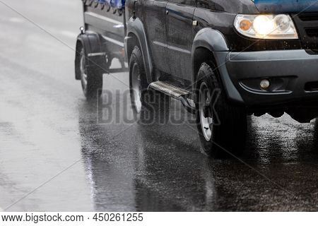 Black Offroad Car With Hindcarriage Behind On Wet Asphalt Road At Rainy Day With Water Splashes Unde