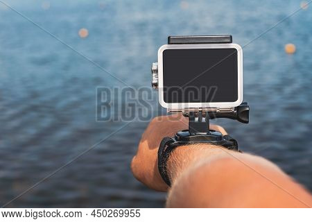 Waterproof Action Camera With Mounts On A Man's Hand. Against The Backdrop Of The Blue Water Of The