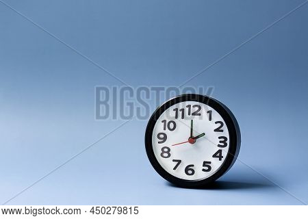 Black Alarm Clock Isolated On Blue Background. The Clock Set At 2 Oclock.