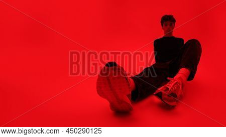 Young people and emotions. Full legth shot of a handsome moody guy sitting on the floor. Bright red background with red light. Copy space.