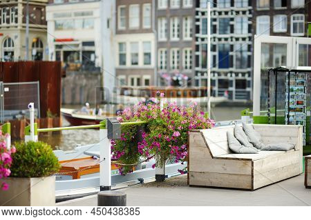 Famous Canals Of Amsterdam, Netherlands. Sitting Area Decorated With Flowers On A Wooden Terrace. Ty