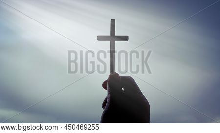 Hand Holding Holy Cross With Bright Shining Light From Sky.