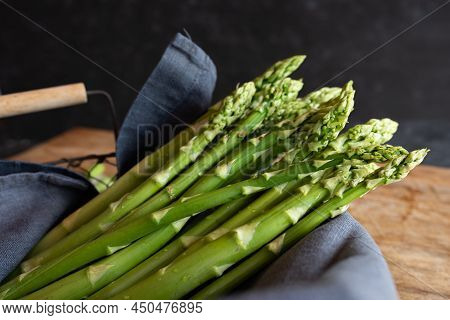 Bunch Of Raw Green Asparagus In A Basket On A Wooden Table. Seasonal Vegetables For A Healthy Nutrit