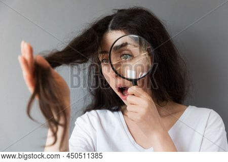 Portrait Of A Young Shocked Caucasian Woman Examining The Dry Tips Of Her Hair Through A Magnifying 