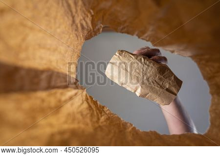 A Hand Places A Paper-wrapped Lunch In A Paper Bag. A Mature Man's Hand Holds The Food With Him Over