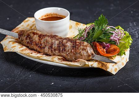 On A Kitchen Wooden Cutting Board, Grilled Beef Kebab Lula, Bowl With Ketchup Sauce, On A Black Isol