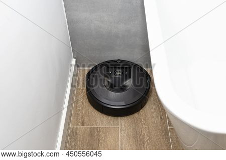A Modern Robotic Vacuum Cleaner Cleans The Ceramic Tiles In The Bathroom Next To The Bath, An Autono