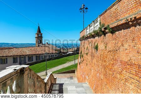 View of old brick wall, houses and belfry under blue sky in small town of Govone in Piedmont, Northern Italy.