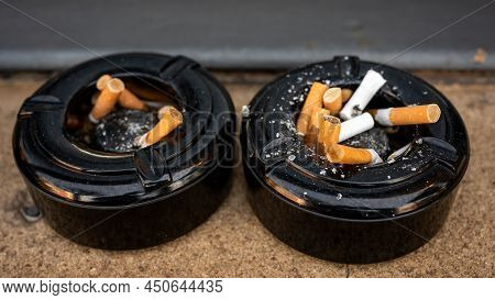 Cigarette In Ashtray. Cigarette Ends In Two Black Ashtrays. Bad Habit.