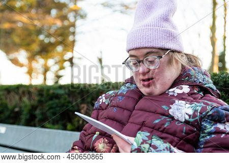 Outdoor Portrait Of A 39 Year Old White Woman With The Down Syndrome Looking At Printed Pictures