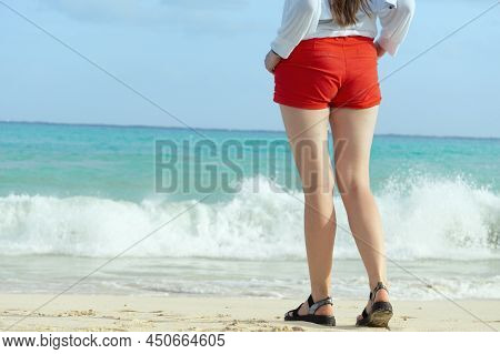 A Close Up Partial Shot On A Girl's Legs Wearing Shorts And Sandals Walking Towards The Sea On The B