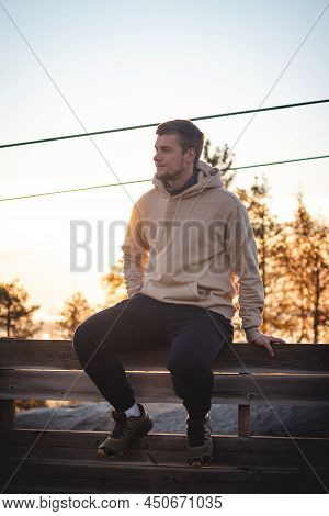 Male Model In A Beige Sweatshirt Sits On Top Of Vuokatinvaara Mountain, In The Kainuu Region, Finlan