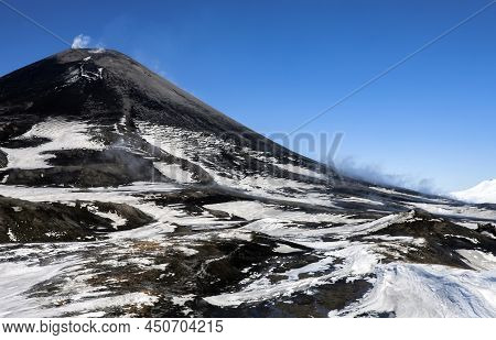 Volcanic Landscape With Dark Cone Of An Active Asian Volcano And White Smoke Against Blue Sky. View 
