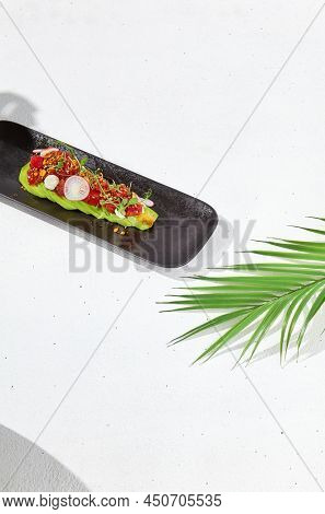 Modern food - tuna tartare on sliced avocado in black plate. Avocado starter with tuna and radish in asian style. Contemporary asian dish. Healthy food with avo and marinated fish on white background