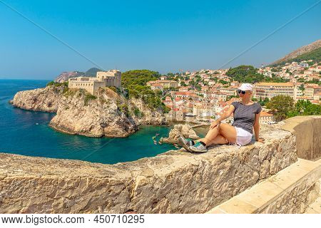 Woman Sitting On Top Walls Of Dubrovnik City Of Croatia. Looking Fort Lovrijenac Fortress, Over The 