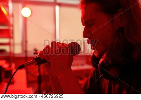 Partial Image Of Emotional Male Singer Singing Song In Microphone At Blurred Red Home. Concept Of Do