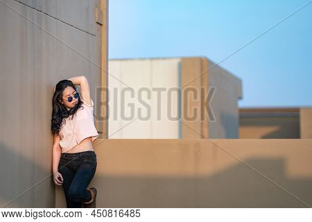 A Cute Asian Woman Stands Up And Raise Elbow Up Against The Wall And Wears Blue Sunglasses At The Ro