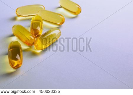 Yellow Softgels Lie On A Violet Surface. Fish Oil.  Vitamins And A Healthy Lifestyle. Background Or 