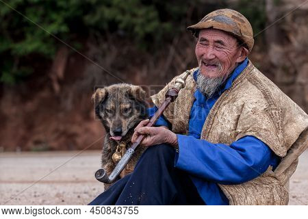 Yunnan, China - March 5, 2012: Portrait Of An Elderly Chinese Bearded Man With Dog Smiling While Smo