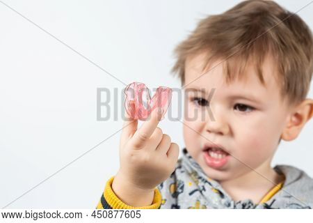 Cute Little Caucasian Boy With Blond Hair Is Holding A Pink Dental Myofunctional Trainer On White Th