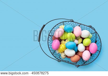 Metal Basket With Multicolored Painted Easter Eggs On Blue Paper Background. Flat Lay  Top View With