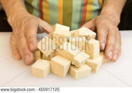 A Person In The Kitchen Wearing A Green Apron Prepares The Meal By Cutting A Block Of Tofu Into Squa