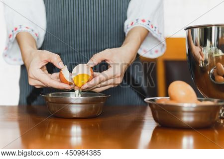 Female Baker With Apron Cracking An Egg Prepare For Baking On Wooden Table