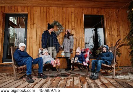 Big Young Family With Four Kids On The Terrace Of A Wooden House In Winter Day.