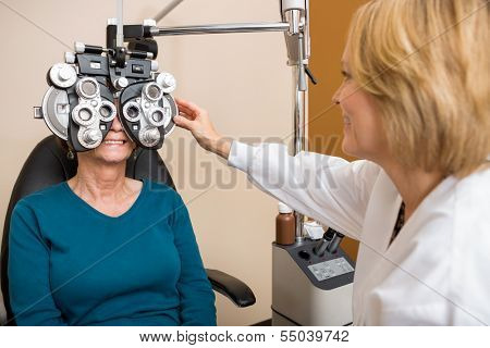 Female optician examining senior patient's vision with phoropter